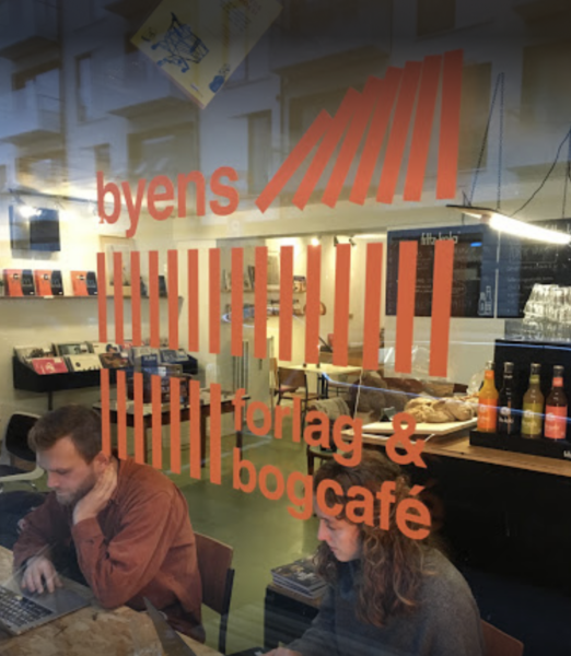 To personer sidder og arbejder set gennem vinduet på Byens Forlags bogcafe i Aarhus.