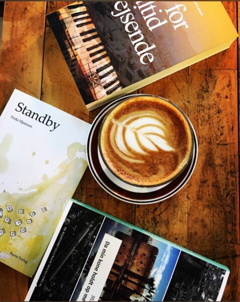 Kaffe med latte-art på bord ved siden af tre bøger.